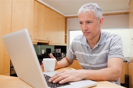 simsearch:400-05749531,k - Man using a laptop while drinking coffee in a kitchen Stock Photo - Budget Royalty-Free & Subscription, Code: 400-05749525