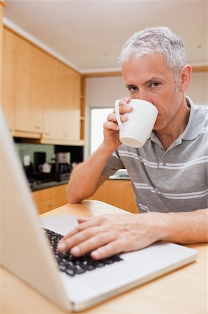 simsearch:400-05749531,k - Portrait of a man using a laptop while drinking tea in a kitchen Stock Photo - Budget Royalty-Free & Subscription, Code: 400-05749534