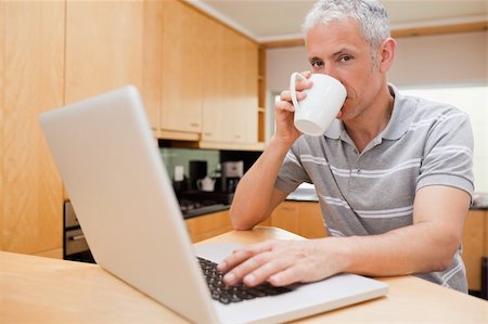 simsearch:400-05749531,k - Man using a notebook while drinking coffee in a kitchen Stock Photo - Budget Royalty-Free & Subscription, Code: 400-05749536