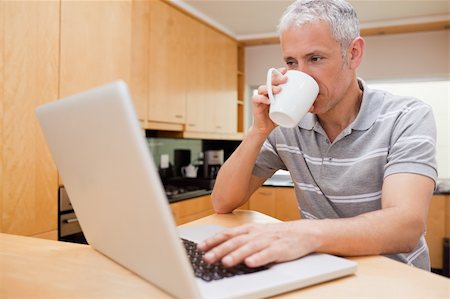 simsearch:400-05749531,k - Happy man using a notebook while drinking coffee in a kitchen Stock Photo - Budget Royalty-Free & Subscription, Code: 400-05749538