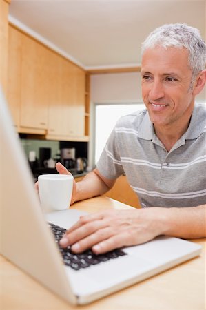 simsearch:400-05749531,k - Portrait of a man using a notebook while drinking coffee in a kitchen Stock Photo - Budget Royalty-Free & Subscription, Code: 400-05749532