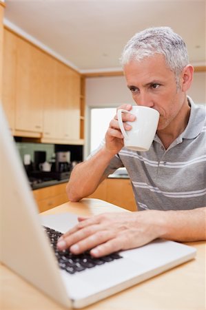 simsearch:400-05749531,k - Portrait of a man using a laptop while drinking coffee in a kitchen Stock Photo - Budget Royalty-Free & Subscription, Code: 400-05749533