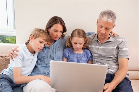 simsearch:400-05749624,k - Family sitting on a sofa using a laptop in a living room Stock Photo - Budget Royalty-Free & Subscription, Code: 400-05749596