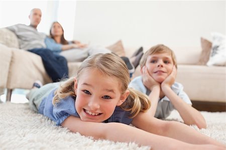 simsearch:400-05749645,k - Siblings lying on a carpet while their parents are sitting on a sofa Stock Photo - Budget Royalty-Free & Subscription, Code: 400-05749625