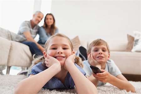 simsearch:400-05749624,k - Siblings watching television with their parents on the background in a living room Stock Photo - Budget Royalty-Free & Subscription, Code: 400-05749627