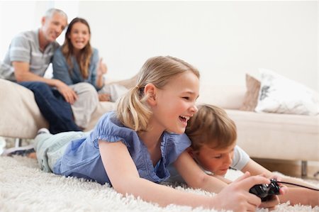 simsearch:400-05749624,k - Siblings playing video games with their parents on the background in a living room Stock Photo - Budget Royalty-Free & Subscription, Code: 400-05749628