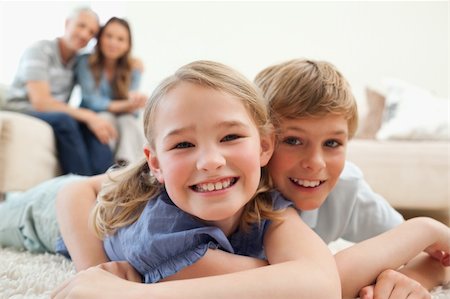 simsearch:400-05749624,k - Happy siblings posing on a carpet with their parents on the background in a living room Stock Photo - Budget Royalty-Free & Subscription, Code: 400-05749638