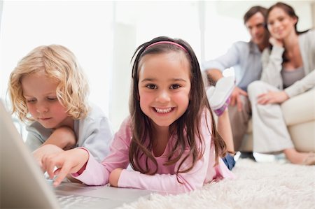 family lying on carpet - Siblings using a laptop while their parents are in the background in a living room Stock Photo - Budget Royalty-Free & Subscription, Code: 400-05749693