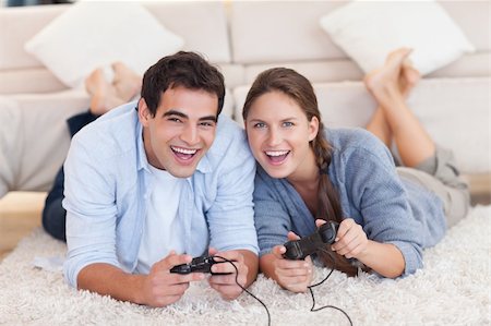 simsearch:400-05740058,k - Delighted couple playing video games while lying on a carpet Photographie de stock - Aubaine LD & Abonnement, Code: 400-05740056