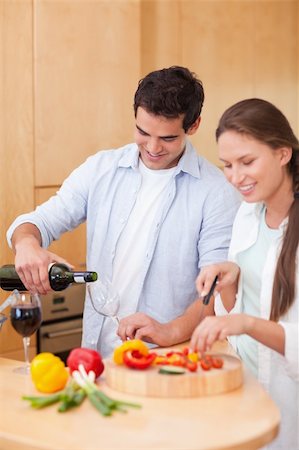 Portrait of a young man pouring a glass of wine while his wife is cooking in their kitchen Photographie de stock - Aubaine LD & Abonnement, Code: 400-05740095