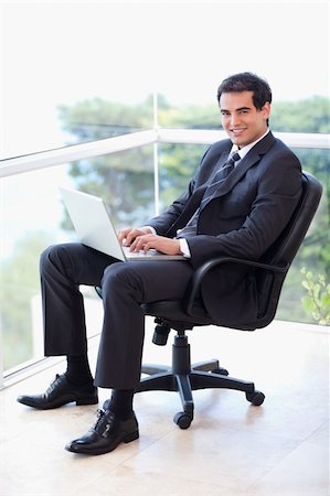 simsearch:400-07514126,k - Portrait of a young businessman sitting on an armchair working with a laptop in his office Fotografie stock - Microstock e Abbonamento, Codice: 400-05740178