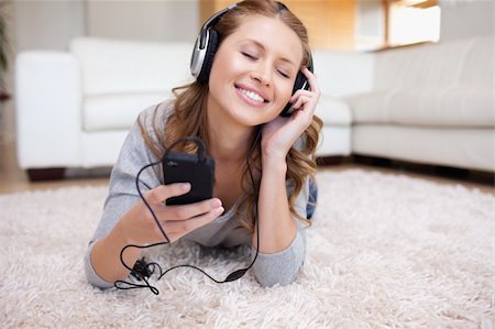 Smiling young woman lying on the carpet listening to music Stock Photo - Budget Royalty-Free & Subscription, Code: 400-05740903