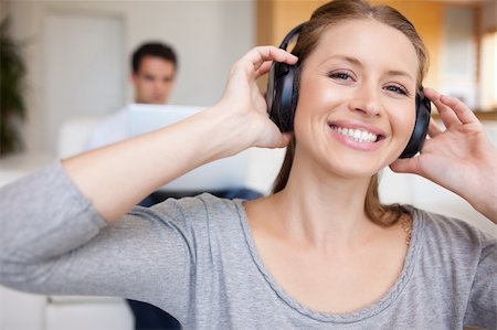 simsearch:400-05209351,k - Smiling woman with headphones on with man sitting behind her on the sofa Stock Photo - Budget Royalty-Free & Subscription, Code: 400-05740926