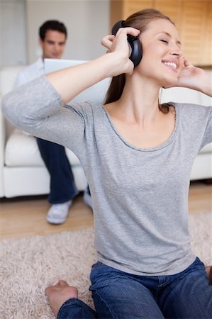 simsearch:400-05209351,k - Young woman with earphones on the carpet and man behind her on the sofa Stock Photo - Budget Royalty-Free & Subscription, Code: 400-05740927