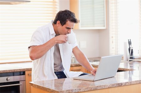 simsearch:400-05749531,k - Young man with coffee and laptop in the kitchen Stock Photo - Budget Royalty-Free & Subscription, Code: 400-05741084