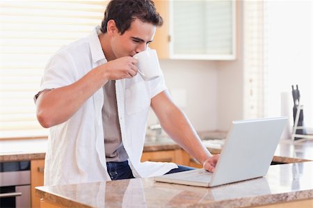 simsearch:400-05749531,k - Young man drinking some coffee while working on his laptop in the kitchen Stock Photo - Budget Royalty-Free & Subscription, Code: 400-05741085