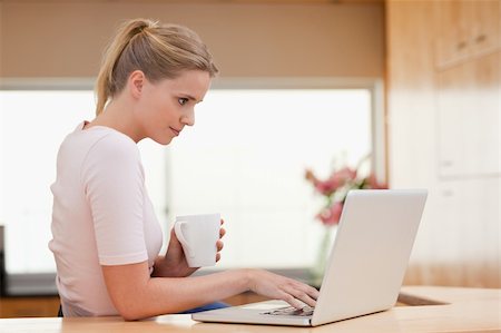 simsearch:400-05741872,k - Woman using a laptop while drinking a cup of a tea in her kitchen Stock Photo - Budget Royalty-Free & Subscription, Code: 400-05741877