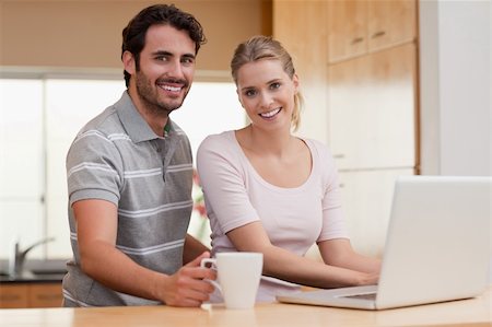 simsearch:400-05741872,k - Smiling couple using a notebook while having coffee in their kitchen Stockbilder - Microstock & Abonnement, Bildnummer: 400-05741873