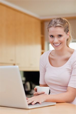 simsearch:400-05741872,k - Portrait of a woman using a laptop while drinking coffee in her kitchen Foto de stock - Super Valor sin royalties y Suscripción, Código: 400-05741888