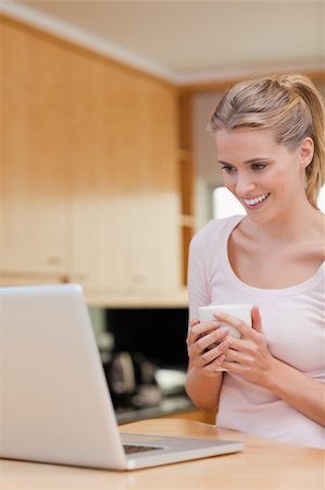 simsearch:400-05741872,k - Portrait of a young woman using a laptop while drinking coffee in her kitchen Stock Photo - Budget Royalty-Free & Subscription, Code: 400-05741889