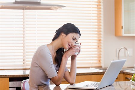 simsearch:400-05741872,k - Lovely woman using a laptop while drinking a cup of a tea in her kitchen Stock Photo - Budget Royalty-Free & Subscription, Code: 400-05742716