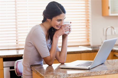 simsearch:400-05741872,k - Lovely woman using a laptop while drinking a cup of a coffee in her kitchen Stockbilder - Microstock & Abonnement, Bildnummer: 400-05742717