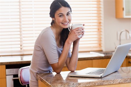 simsearch:400-05741872,k - Charming woman using a laptop while drinking a cup of a coffee in her kitchen Stock Photo - Budget Royalty-Free & Subscription, Code: 400-05742718