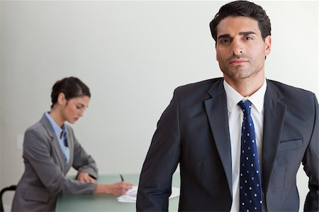 simsearch:400-04287075,k - Handsome businessman posing while his colleague is working in an office Fotografie stock - Microstock e Abbonamento, Codice: 400-05742792