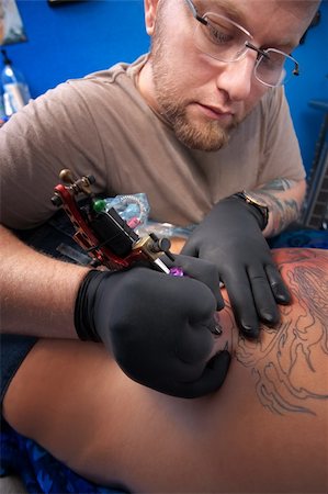 Caucasian Tattoo technician engraves a tattoo on woman's back Fotografie stock - Microstock e Abbonamento, Codice: 400-05754656