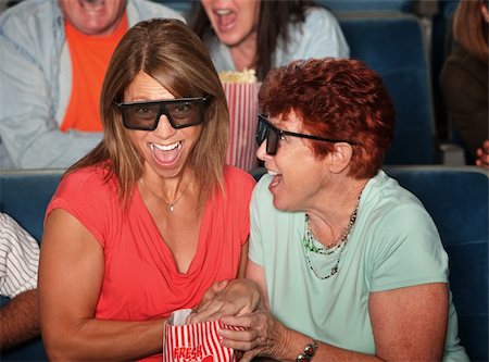 simsearch:400-06138368,k - Laughing women in theater with bag of popcorn Fotografie stock - Microstock e Abbonamento, Codice: 400-05754659