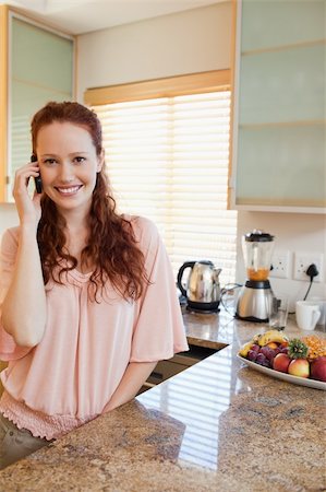 simsearch:400-05751258,k - Smiling woman on the phone next to the kitchen counter Stock Photo - Budget Royalty-Free & Subscription, Code: 400-05751262