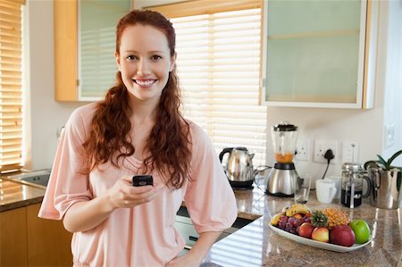 simsearch:400-05751258,k - Smiling woman holding her cellphone in the kitchen Stock Photo - Budget Royalty-Free & Subscription, Code: 400-05751462
