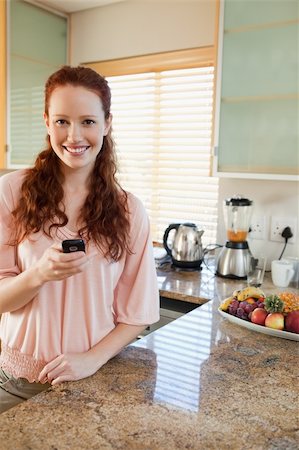 simsearch:400-05751258,k - Smiling woman in the kitchen with her cellphone Stock Photo - Budget Royalty-Free & Subscription, Code: 400-05751463