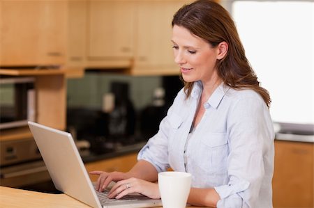 simsearch:400-05749531,k - Woman with cup in the kitchen using her laptop Stock Photo - Budget Royalty-Free & Subscription, Code: 400-05751624