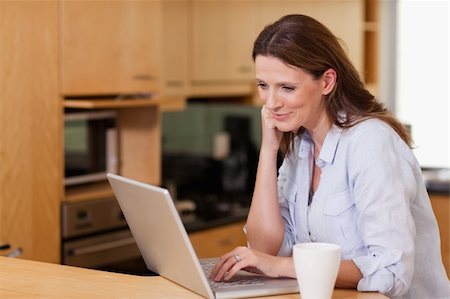 simsearch:400-05749531,k - Smiling woman in the kitchen looking at her laptop Stock Photo - Budget Royalty-Free & Subscription, Code: 400-05751628