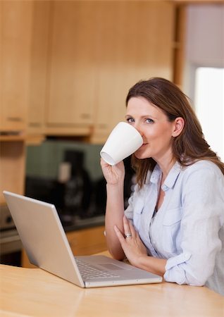 simsearch:400-05741872,k - Woman taking a sip of coffee next to her laptop Foto de stock - Super Valor sin royalties y Suscripción, Código: 400-05751630