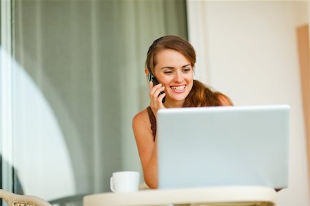 Smiling young woman on terrace speaking cell phone and looking on laptop Stock Photo - Budget Royalty-Free & Subscription, Code: 400-05753455