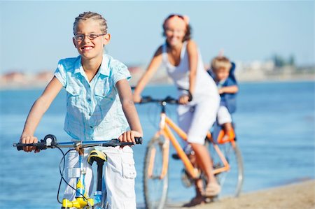 parent and teen bikes - Cute girl with her mother and brother ride bikes along the beach. Focus on girl Stock Photo - Budget Royalty-Free & Subscription, Code: 400-05875949