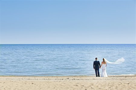 happy wedding couple standing on beach and holding hands. The bride veil flutters Foto de stock - Super Valor sin royalties y Suscripción, Código: 400-05875952