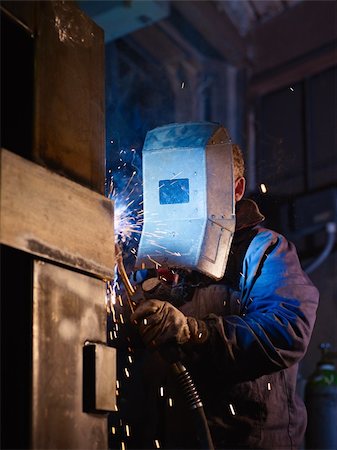 simsearch:6109-08689632,k - Manual worker in steel factory using welding mask, tools and machinery on metal. Vertical shape, side view, waist up Foto de stock - Super Valor sin royalties y Suscripción, Código: 400-05880686