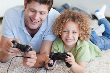 Happy boy and his father playing video games while lying on a carpet Stock Photo - Budget Royalty-Free & Subscription, Code: 400-05894832