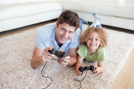 Smiling boy and his father playing video games while lying on a carpet Stock Photo - Budget Royalty-Free & Subscription, Code: 400-05894833