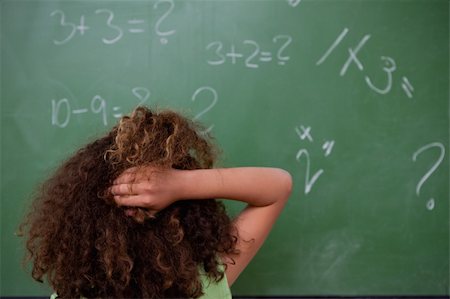 Schoolgirl thinking about mathematics while scratching the back of her head in front of a blackboard Stock Photo - Budget Royalty-Free & Subscription, Code: 400-05896431