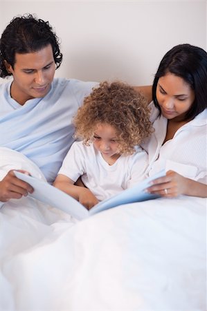 simsearch:400-05751566,k - Young family sitting on the bed reading a story Stock Photo - Budget Royalty-Free & Subscription, Code: 400-05897692