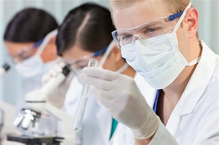 A male medical or scientific researcher or doctor looking at a test tube of clear liquid in a laboratory with microscopes and his female colleagues behind him Stock Photo - Budget Royalty-Free & Subscription, Code: 400-05891612