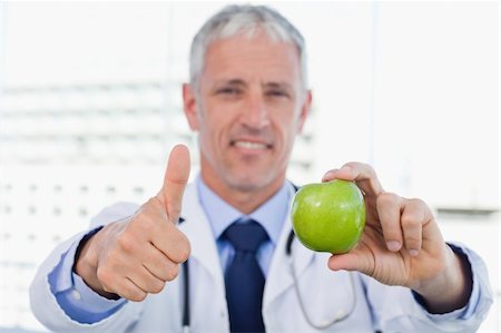 simsearch:400-05728490,k - Doctor showing an apple with the thumb up in his office Photographie de stock - Aubaine LD & Abonnement, Code: 400-05892410