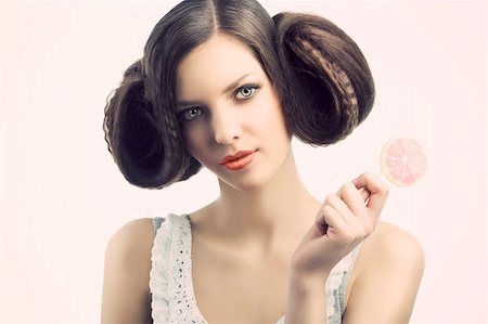 young beautiful brunette with a creative luxury hair style and a colored lollipop. She looks in to the lens and has the face slightly folded at right. She tales the lollipop with left hand. Stock Photo - Budget Royalty-Free & Subscription, Code: 400-05918481