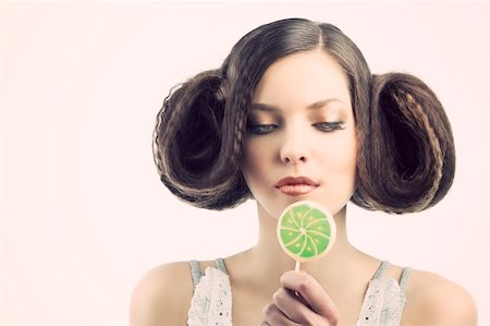 young beautiful brunette with a creative luxury hair style and a colored lollipop. she looks the lollipop and takes that near the mouth. Stock Photo - Budget Royalty-Free & Subscription, Code: 400-05918482