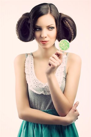 young beautiful brunette with a creative luxury hair style and a colored lollipop, she looks the lollipop and takes that with the left hand. Stock Photo - Budget Royalty-Free & Subscription, Code: 400-05918483