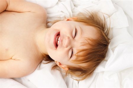 Happy child laughing and laying in white sheets Stock Photo - Budget Royalty-Free & Subscription, Code: 400-06065819